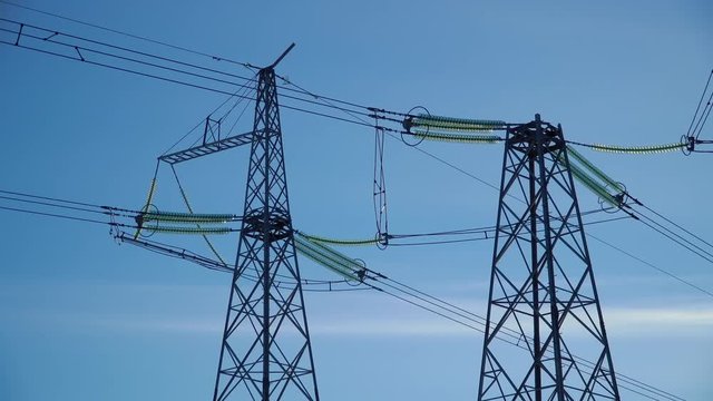 Close up: top of two high voltage power transmission tower and electricity pylon with wires against blue sky
