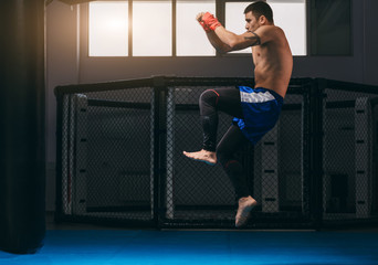 Martial arts of Muay Thai, Thai Boxing, Muay Thai. Barefoot Fighter training indoors dressed in blue boxer shorts and having his fists protected with red bandage.