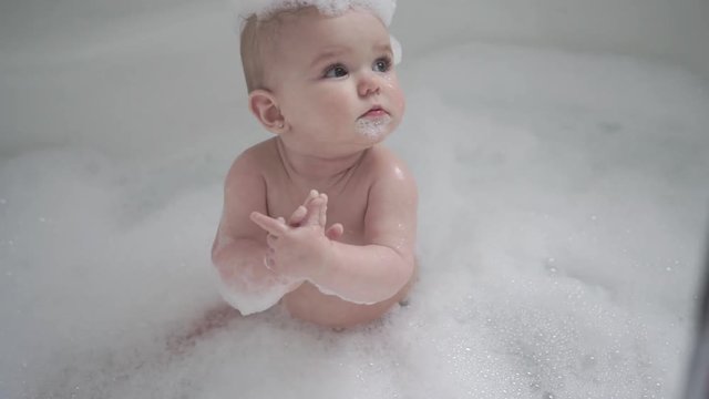 A Baby girl bathes in a bath with foam and soap bubbles