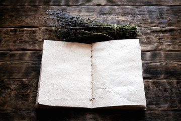 Dried lavender flower branch and a blank aromatherapy recipe book mock up on a wooden table background with copy space. Herbal medicine concept.