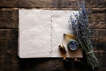Dried lavender flower branches, lavender essential oil bottles and a blank aromatherapy recipe book...