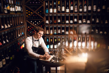 Elegant wine seller holding a bottle of wine and reading label in a wine store. Choosing wine according to its origin country and vintage.