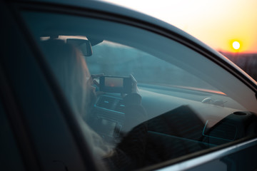 Young girl taking photo of sunset from car.