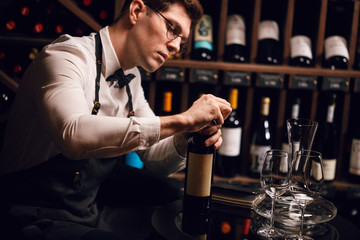 Bartender opening a wine bottle with corkscrew in restaurant with wine shelves.