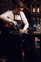 Elegant young sommelier with bow tie uncorking bottle of wine in wine boutique. Wine tasting social event.