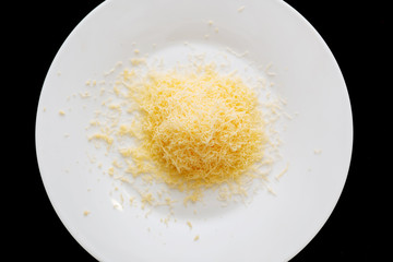 Shredded grated cheese in a large white ceramic plate on a black background