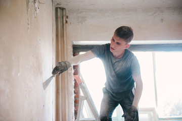 A man removes old paint from the ceiling with a spatula