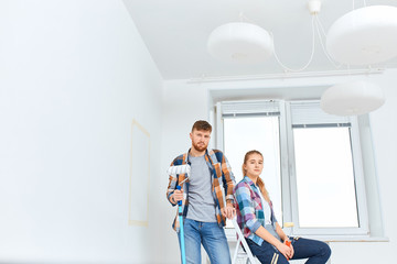 Portrait of caucasian attractive couple in checkered shirts standing , holding paint roller and brush, looking at camera.