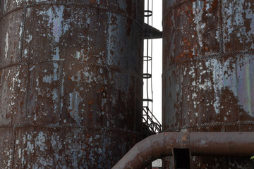View of sky and escape ladder between two rusting metal blast furnaces, steel industry, horizontal aspect