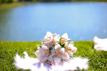 White bouquet of Orchid flowers lying on the grass against the lake
