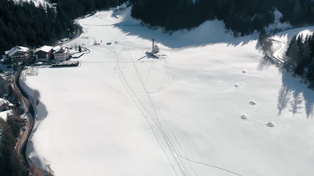 Aerial Reveal Shot of St. Johann in Ranui Church Down in the Valley and Odle Mountain Group on the Background in Dolomites, Italy, in Winter