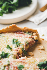 A piece of homemade cheese quiche or pie sprinkled with parsley on gray concrete background. Vintage toned. French cuisine