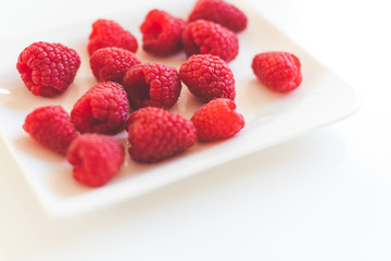 Raspberries on white plate, on white background