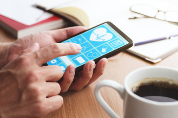 Online healthcare app on smartphone screen. Closeup of male hands touching smartphone screen at table. - obrazy, fototapety, plakaty