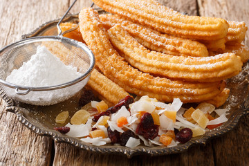 High-calorie deep-fried churros with powdered sugar and candied fruit close-up on a plate. horizontal