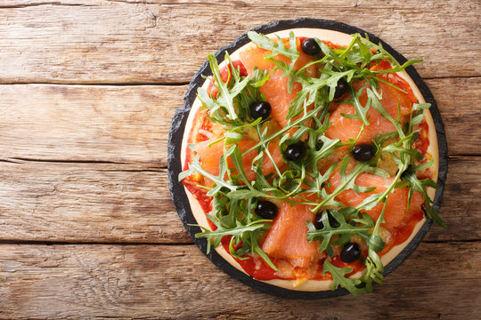 Recipe for delicious Italian pizza with salmon, arugula, black olives and mozzarella cheese close-up. horizontal top view