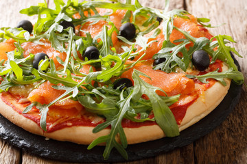 Salmon pizza with fresh arugula, black olives and cheese closeup. horizontal