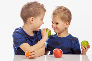 Boys brothers are sitting at the table, laughing and feeding each other fruit, close-up. Isolated...