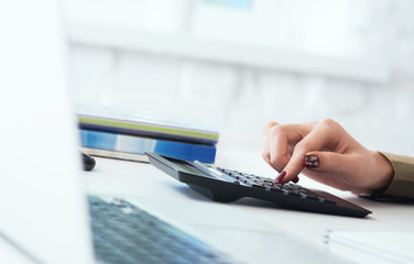 Close up of woman hands with calculator counting and taking notes to laptop. Job of an accountant...