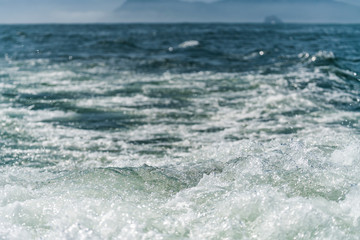 A deep blue sea with island in distance with medium water wave ripple.