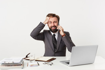 Everything goes wrong, OMG, it's a disaster! Dressed in a suit respectable office worker sitting at desktop grasping his head panics, nervous, is in a difficult situation, holding a phone near his ear
