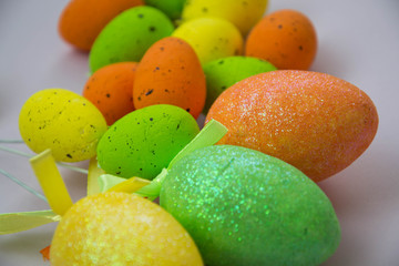 Close up of colorful Easter eggs on a pale pink table, Easter holiday concept, traditions, egg hunt decoration, yellow, green and orange small eggs