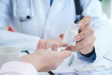Female doctor hands gives jar of pills to patient hand closeup.