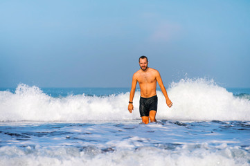young attractive and happy man with beard and swimming trunks at tropical paradise desert beach alone playful and cheerful in sea water enjoying Summer holidays