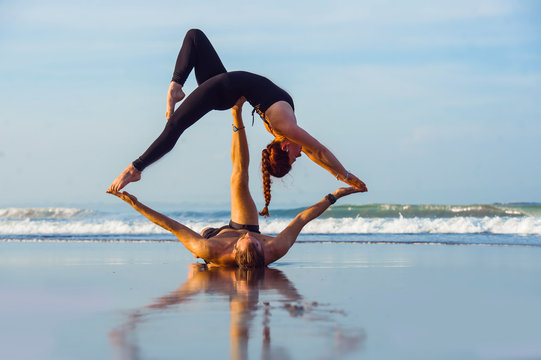 young attractive and beautiful acrobat couple practicing acroyoga exercise concentrated keeping balance practiing yoga on the beach in relaxation and meditation concept