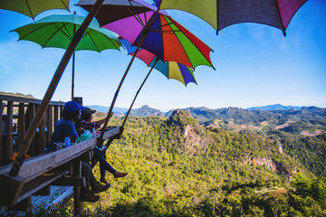 Tourists asian couple sitting eat noodle on the wooden platform and looking scenic view of beautiful nature mountains at Ban Jabo,Mae Hong Son, Thialand.