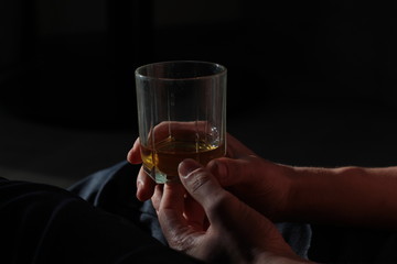 on a dark background are male hands holding a glass with a drink