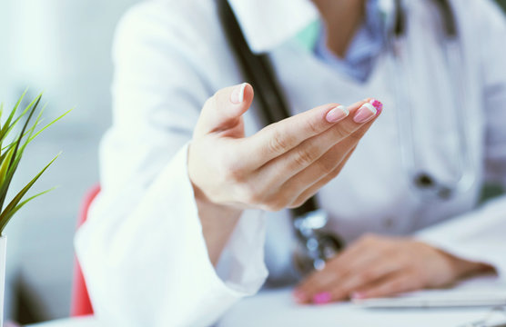 Female Doctor Explaining Patient Symptoms Or Asking A Question As They Discuss Together In A Consultation. Just Hands Over The Table.