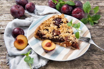 Piece of Plum Cake on a plate with ripe plums and mint leaves, wooden table
