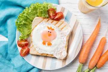 Funny toast with fried egg in a shape of chicken and fresh carrots, healthy food for kids Easter idea, top view