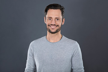 Young attractive man with a grey t-shirt smiling happy in front of a grey background