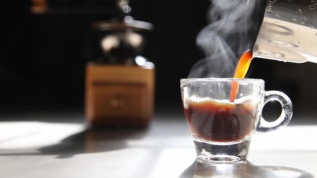 Traditional home brew espresso coffee pouring into a small cup with grinder on the dark background by the morning light