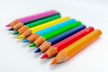 Multi colored bunch of assorted rainbow color pencil line up in a row close together side by side arranged in white background, flat lay. Selective focus blur image. Back to school creative concept