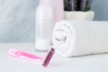 Women's shaving razor with shampoo, towel and antiperspirant on the bathroom background. Removal of unwanted hair. Spa and female treatments. Epilation concept
