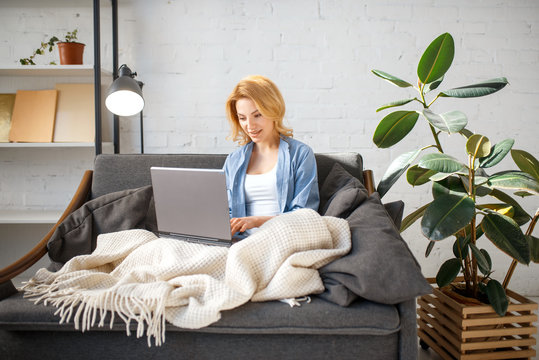 Young Woman Under A Blanket Using Laptop On Couch