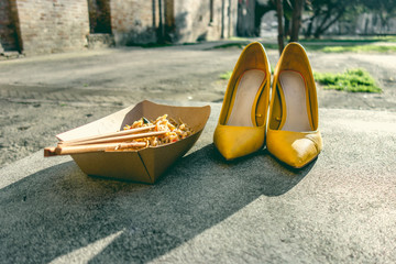 A pair of yellow girl's shoes with the remnants of a portion of noodle and related Chinese chopsticks. Women freedom barefoot concept.
