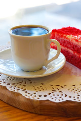 A cup of coffee and red cake on a wooden plank and a white napkin.