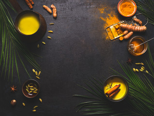 Healthy food background with detox turmeric milk preparation and ingredients on dark background, top view. Copy space. Healthy hot beverages concept. Natural immune boosting