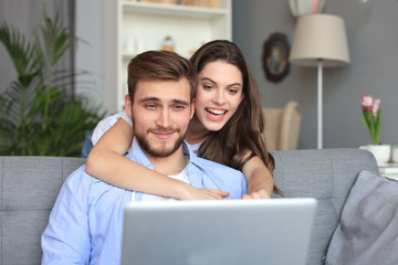 Young couple doing some online shopping at home, using a laptop on the sofa.