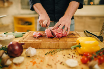 Male person with knife cuts raw meat into slices