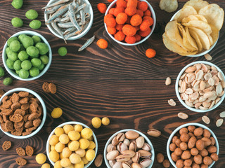 Assortment of different snack for beer, wine, party. Peanuts in coconut glaze, green vasabi, red spicy chilli, yellow cheese glaze, chips, pistachio, crackers, fish on brown wooden table. Copy space