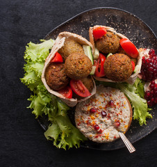 Traditional homemade hummus, falafel in pita and tahini with fresh tomato salad and spices on a black chopping Board. Jewish and Arabic cuisine. The concept of vegetarian food. The view from the top