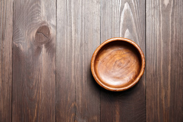 Empty wooden bowl on brown background. Round salad-bowl on wooden table. Top view