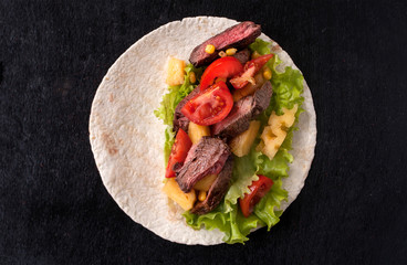 Cornbread with beef, vegetables and pineapples and corn grains on a wooden kitchen Board. Food preparation. Taco al pastor on a black wooden Board. Top view with copy space