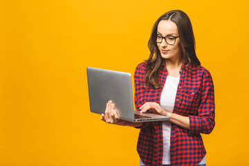 Naklejka premium Young happy smiling woman in casual clothes holding laptop and sending email to her best friend. Isolated against yellow background.