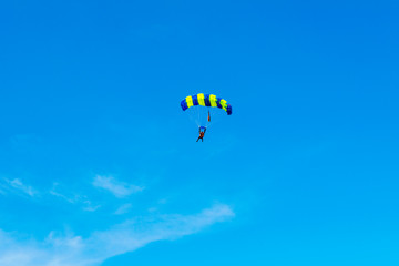 Male skydiver flies under the wing of the parachute, descending and coming in to land closer to the ground on a background of blue sky, white clouds